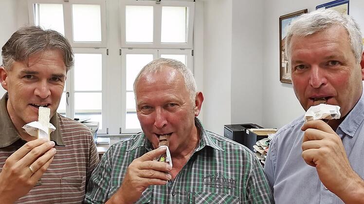 Eberns dritter Bürgermeister Werner Riegel (Mitte) fair-nascht zusammen mit seinen Amtskollegen Harald Pascher (links) und Jürgen Hennemann (recht) einen Schokoriegel aus fairem Handel, aus dem Naschkorb mit fairen Süßigkeiten, der ab sofort im Bürgermeisterbüro für Besucherinnen und Besucher bereitsteht.  pr