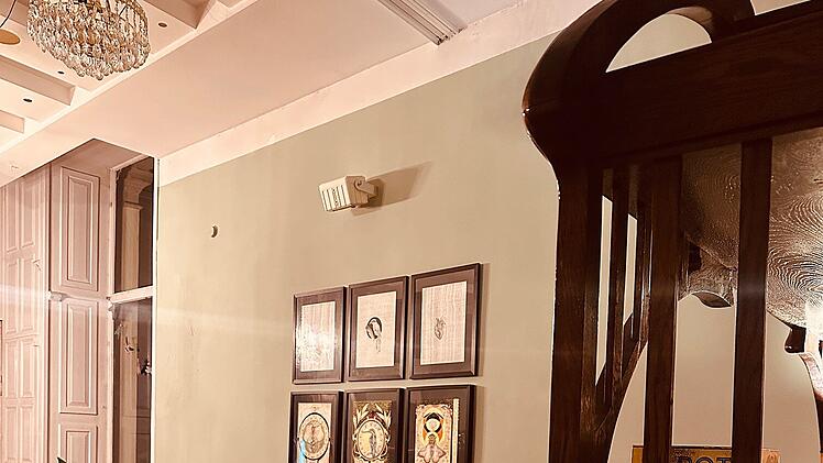 Gem&uuml;tliches Caf&eacute; mit Holzboden, roter Couch und Tisch, geschm&uuml;ckt mit Kunstwerken an der Wand. Warme Beleuchtung und stilvolle Einrichtung schaffen eine einladende Atmosph&auml;re.