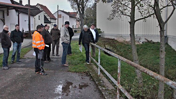 Sehr wackelig ist das Geländer an dem Feldweg über die Baunach gegenüber dem Friedhof in Gemeinfeld, wie Reinhold Klein (Zweiter von rechts) Bürgermeister Hermann Niediek (rechts) und den Teilnehmern der Begehung zeigt. Der Graben rechts hinten sollte verrohrt werden.H. Will