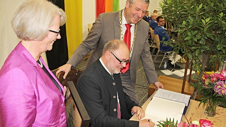 Bürgermeister Jürgen Hennemann (rechts) und die Gattin des Altbürgermeisters, Christiane Herrmann (links) schauen zu, wie der Geehrte sich in das Goldene Buch der Stadt Ebern einträgt.