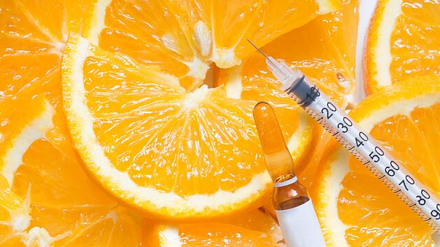 Hochdosierte braune Vitamin-C-Ampulle zur Injektion mit Spritze auf frischen saftigen Orangenscheiben. Konzept der Vitamin-/Mineralienerg&auml;nzung, Sch&ouml;nheit/Kosmetik