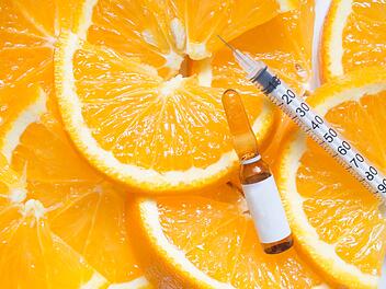 Hochdosierte braune Vitamin-C-Ampulle zur Injektion mit Spritze auf frischen saftigen Orangenscheiben. Konzept der Vitamin-/Mineralienergänzung, Schönheit/Kosmetik