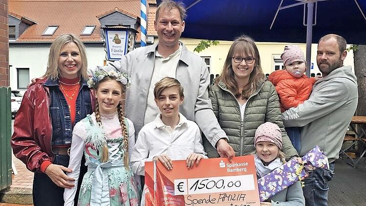 Scheck&uuml;bergabe mit (v. l.) Verena Eichfelder von Kachelofen-Premiumpartner Kaufhaus Schrill, ihren beiden Kindern Greta und Gabriel, Sebastian Linz, Amilias Mutter Sonja, Amilias Schwester Mathilda, Amilia und ihrem Vater Michael.