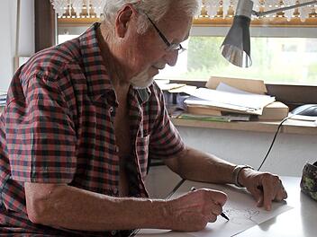 Heinz Körner sitzt an seinem kleinen Schreibtisch und malt eine Figur.  Foto: Sarah Stieranka
