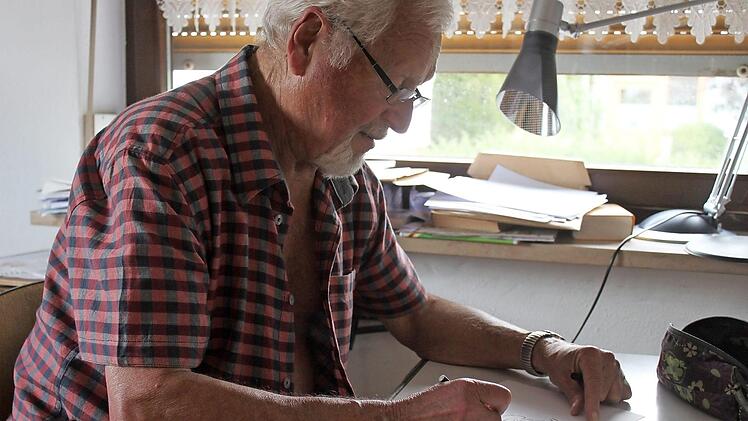 Heinz Körner sitzt an seinem kleinen Schreibtisch und malt eine Figur.  Foto: Sarah Stieranka