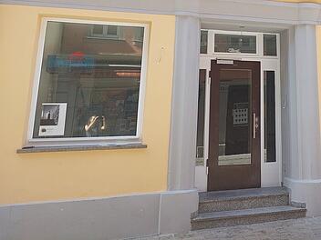 Helles Gebäude mit einem großen Fenster und Glastür, gelbe Fassade, grauer Sockel. Es könnte sich um eine Bar in Bamberg handeln, über die Gerüchte kursieren, wie von inFranken.de berichtet.