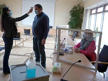 Wahlleiterin Eva Fröhlich demonstriert beim Zweiten Bürgermeister Karl-Heinz Hertlein die Temperaturmessung, Karin Süß sitzt am Platz eines Wahlhelfers.     Foto: Richard Sänger