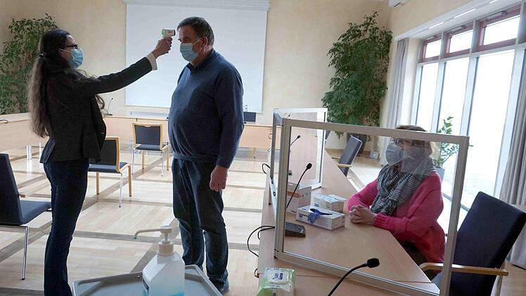 Wahlleiterin Eva Fröhlich demonstriert beim Zweiten Bürgermeister Karl-Heinz Hertlein die Temperaturmessung, Karin Süß sitzt am Platz eines Wahlhelfers.     Foto: Richard Sänger