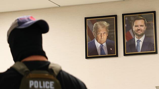 Ein New Yorker Bundesagent geht an Port&auml;rts von US-Pr&auml;sident Trum und Vizepr&auml;sident JD Vance vorbei. Die US-Regierung geht konsequent gegen Einwanderer ohne Aufenthaltstitel vor.
