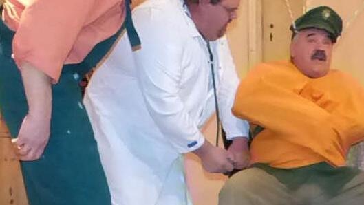 . Archibald Hirnbrand, dargestellt vonThomas Ittner (Mitte), haut dem in der Zwickmühle steckenden, gefesselten Dorfgendarmen Waldemar Hasenschreck (Willi Pöhlmann) eine Beruhigungsspritze rein. Amüsiert schaut Xaver (Willi Rucker) dem Geschehen zu. Foto: Klaus-Peter Wulf