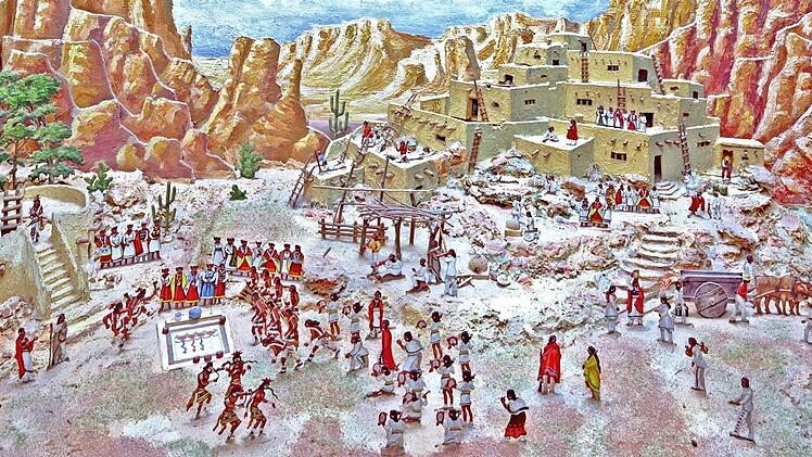 Die terrassierte Lehmsiedlung der Hopi-Indianer mit Tempel und Versammlungsplatz, auf dem der Schlangen-Ritual stattfindet, vorne die Maskentänzer, hinter der Schlangengruben die Priester, rechts Frauen mit Mehlstäubern, um die giftigen Klapperschlangen zu betäuben