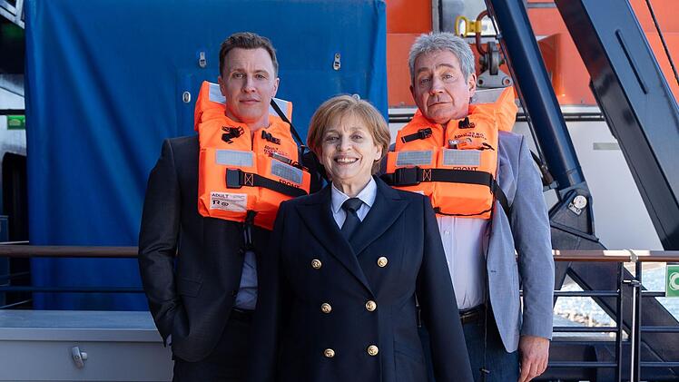 Die Ex-Kanzlerin (Katharina Thalbach) will an Bord eines Kreuzfahrtschiffs den Mord an einem Krimiautor aufklären. Links Bodyguard Mike (Tim Kalkhof), rechts Joachim Sauer (Thorsten Merten).