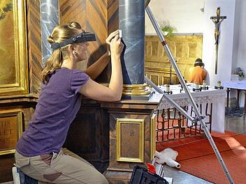 Expertin Annegret Schwarz arbeitet, mit Lupenbrille und Skalpell ausgestattet, an einer Säule des Marienaltars in der Burkardrother Pfarrkirche. Im Hintergrund ist Restaurator Georg Hille aus Oberelsbach zu sehen. Er und sein Team untersuchten Ende August, Anfang September, wie die Kirche früher aussah. Foto: Kathrin Kupka-Hahn