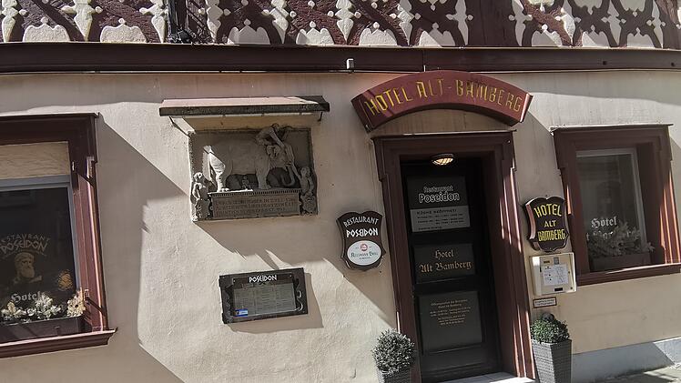 Eingang des "Poseidon" Restaurants in Bamberg. Leere Fassade, geschlossene Tür, Pflanzen an beiden Seiten. Schilder weisen auf Restaurant und Hotel hin. Betreiber sind offenbar verschwunden.