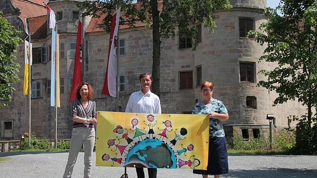 Vor dem Wasserschloss pr&auml;sentierte die Leiterin der Unicef-Arbeitsgruppe Oberfranken, Gisela Schardt, das Plakat f&uuml;r das 14. Unicef-Kinderfest in Mitwitz zusammen mit B&uuml;rgermeister Hans-Peter Laschka und Barbara Laschka (von links ). Foto: Herbert Fischer