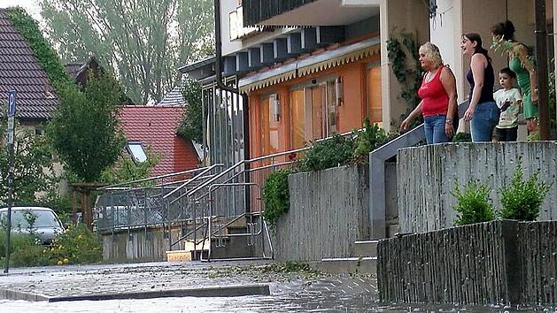 Anwohner schauen auf eine überflutete Straße. Anfang August 2014 zog ein schweres Unwetter über Neunkirchen am Brand. Dabei wurden zahlreiche Bäume entwurzelt, Häuser abgedeckt und mehrere Keller liefen voll Wasser.