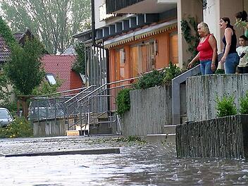 Anwohner schauen auf eine überflutete Straße. Anfang August 2014 zog ein schweres Unwetter über Neunkirchen am Brand. Dabei wurden zahlreiche Bäume entwurzelt, Häuser abgedeckt und mehrere Keller liefen voll Wasser.