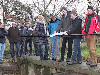 Martin Rottenberger (2. von rechts), Peter Borst (3. von rechts) und Wolf-Dieter Jacob (rechts) erklären den Praktikern aus den Gemeinden vor Ort ihre Pläne zur Einbeziehung des Nudelbachs in den Spielplatz in Hausen. Der soll in absehbarer Zeit saniert werden. Foto: Sabine Herteux