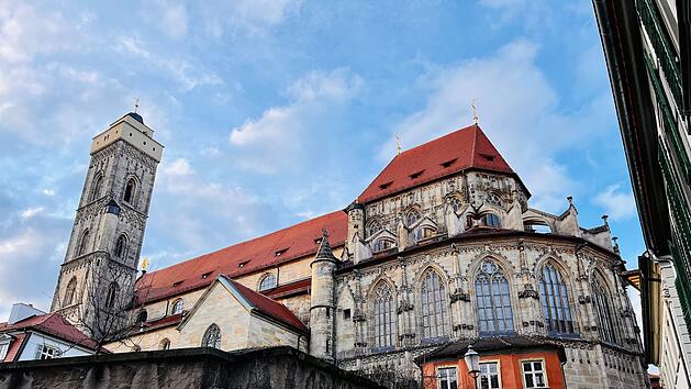 Eine Kirche in Bamberg, zeigt gotische Elemente mit roten Dächern und detaillierten Fenstern. Der Turm erhebt sich majestätisch, eingerahmt von historischem Charme.