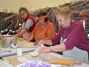 Ein Blick in das Feuerwehrhaus: Hier werden die Kartoffel-Plootze vorbereitet. Thekla Grom (von rechts) rollt den Teig aus, Marga Rost schmiert Kartoffelbrei darauf, und Marianne Metz verfeinert mit einem Schuss Schmiere und Butter. Foto: Kathrin Kupka-Hahn