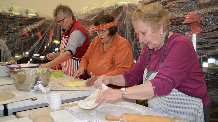 Ein Blick in das Feuerwehrhaus: Hier werden die Kartoffel-Plootze vorbereitet. Thekla Grom (von rechts) rollt den Teig aus, Marga Rost schmiert Kartoffelbrei darauf, und Marianne Metz verfeinert mit einem Schuss Schmiere und Butter. Foto: Kathrin Kupka-Hahn