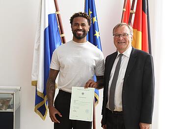 Stolz präsentiert Bryce Taylor (l.) seine Einbürgerungsurkunde, die er aus der Hand von Oberbürgermeister Andreas Starke erhalten hat. Foto: sportpress
