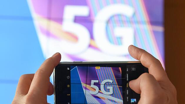Ein Journalist fotografiert vor dem Start der Auktion von 5G-Mobilfunkfrequenzbl&ouml;cken am Mainzer Technik-Standort der Bundesnetzagentur das K&uuml;rzel &laquo;5G&raquo; mit seinem Smartphone.  W&auml;hrend in Deutschland die Frequenzen versteigert werden, haben die St&auml;dte Br&uuml;ssel und Genf den Aufbau des Hochgeschwindigkeitsnetzes gestoppt.Foto: Arne Dedert/dpa