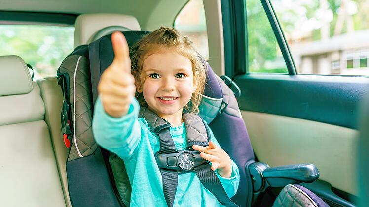 Kleines Kind sitzt im Auto und zeigt den Daumen nach oben, A Small child sitting in a car seat in the car