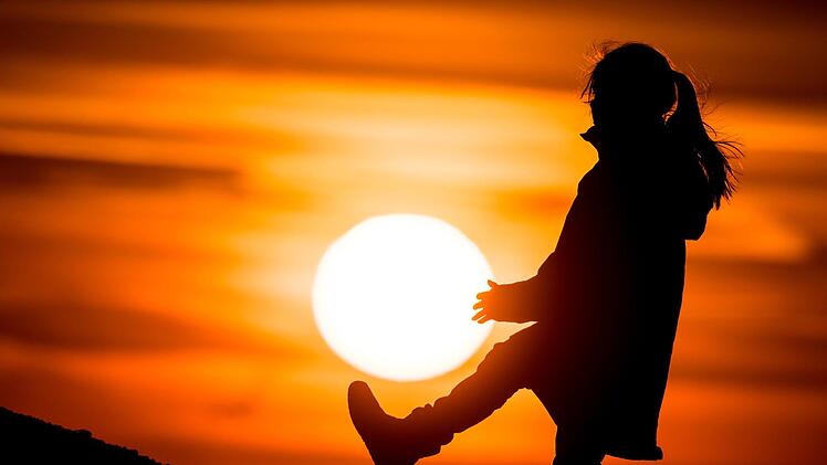 Ein Mädchen spielt im farbenprächtigen Sonnenuntergang nahe Sieversdorf. Am 20. März schiebt sich der Mond vor die Sonne und verdunkelt den Himmel. In Deutschland wird es zwar keine totale Sonnenfinsternis geben wie auf den Färöer-Inseln und Spitzbergen. Leicht duster wird es aber ab etwa 9.30 Uhr schon, so die Experten. Foto: Patrick Pleul/dpa