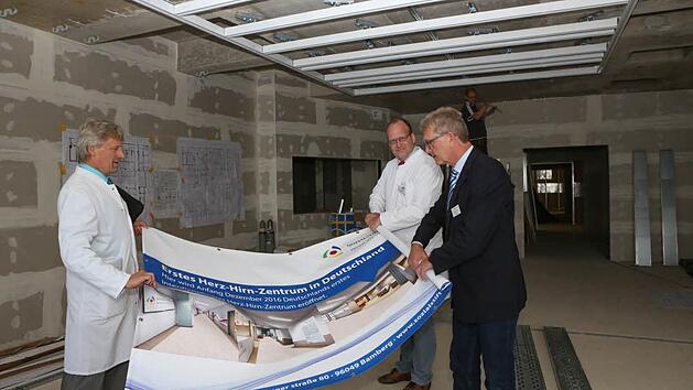 Die Chef&auml;rzte Peter Rieckmann und Martin Braun begehen gemeinsam mit Wolfgang Freitag (Leiter Bau und Technik), regelm&auml;&szlig;ig die Baustelle. Noch m&uuml;ssen sie sich anhand eines Plakats vorstellen, wie das Herz-Hirn-Zentrum einmal aussehen soll. Foto: Barbara Herbst
