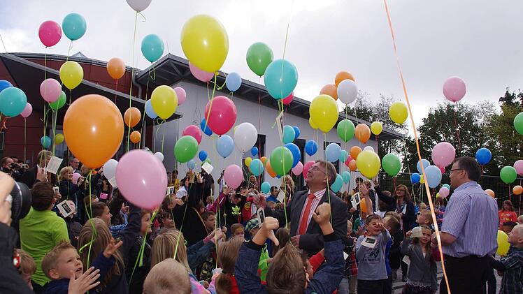 Kinder und Erwachsene lassen vor der Schule Luftballons steigen.