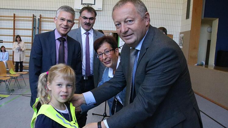 Sparkassen-Vorstand Roland Friedrich, der Nüdlinger Bürgermeister Harald Hofmann, Roswitha Kaufmann von der Saale-Zeitung und Landrat Thomas Bold übergeben ein Sicherheitsdreieck an Erstklässlerin Fabia.  Foto: Ralf Ruppert