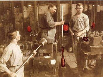 Hart und beschwerlich war die Arbeit der Glasbläser. Im Dreierteam arbeiteten sie an einer der 16 Werkstätten. Das Arbeitsergebnis: 300 Flaschen je Schicht. Die kolorierte Aufnahme entstand um 1925.  Repro: Gerd Fleischmann