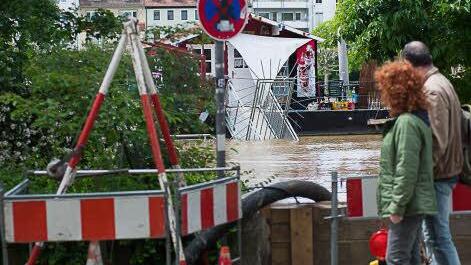 Spaziergänger schauen am Sonntag in Würzburg über das Hochwasser auf ein geschlossenes Hausboot-Cafe. Foto: Tobias Köpplinger
