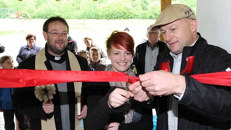 Unter den Augen von Pfarrer Daniel Schuster (l.) und Bürgermeister Claus Schwarzmann schneidet Julia Fronhöfer (m.) bei der Eröffnung des Drügendorfer Jugendtreffs das Band an der Eingangstür durch. Fotos: Erlwein