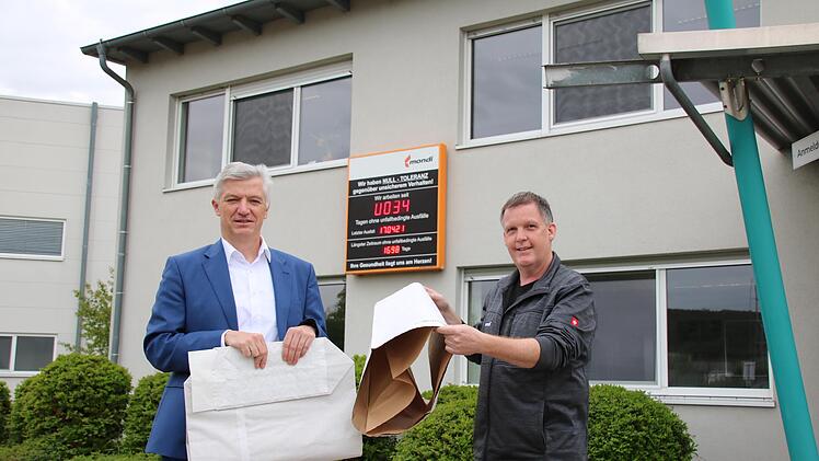 Werkleiter Peter Rüger (rechts) zeigt den ersten Produktionsschritt, in dem mehrere Lagen zu einem Schlauch verklebt werden. Links hält Geschäftsführer Volker Reimer einen fertigen Sack mit Boden. Dahinter die "Mondi-Uhr", die an jedem Standort anzeigt, wann der letzte Unfall im Werk passiert ist. Foto: Ralf Ruppert