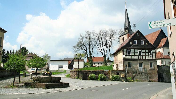 Blick auf die Dreieinigkeitskirche in Weißenbrunn und auf das davor stehende Lerners-Haus. Links davon soll das der Spitzhacke zum Opfer gefallene Schramms-Haus neu aufgebaut werden. Vorne der Dorfbrunnen "Jungferkättl"  Foto: Karl-Heinz Hofmann
