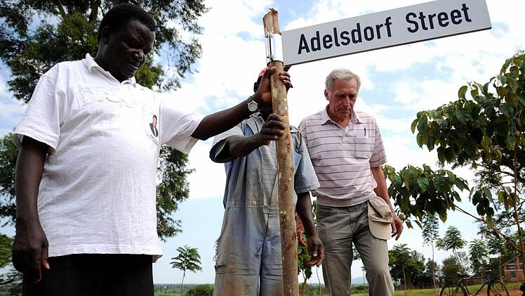Günther Müller befestigt zusammen mit Pfarrer Peter Ssenkaayi das Straßenschild gegenüber der neuen Krankenstation in der Pfarrei Busagula. Foto: Stefan Reinmann
