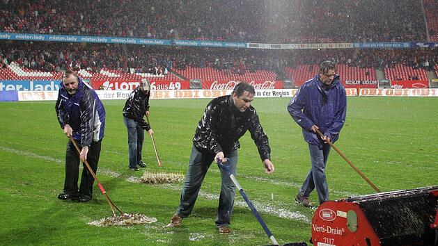 Mit Schneeschiebern, Rechen und einer Drainagewalze  versuchen Helfer, den Rasen vom Wasser zu befreien. imago