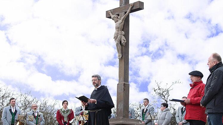 Pater Rudolf Götz OSA (Mitte) segnete das sanierte Feldkreuz am Wanderweg von Münnerstadt nach Fridritt. Rechts der stellvertretende Vorsitzende des Rhönklub-Zweigvereins Münnerstadt, Rainer Kirch, und Bürgermeister Helmut Blank. Im Hintergrund Mitglieder der Musikkapelle Fridritt, die die Feier musikalisch umrahmten.  Foto: Dieter Britz