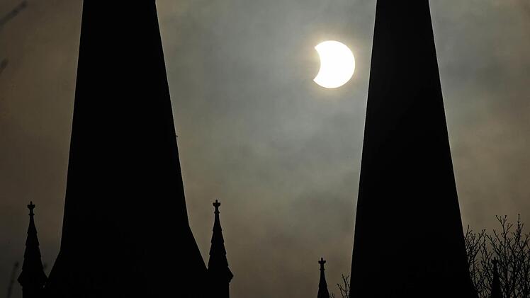 Sichelförmig erscheint die Sonne am 04.01.2011 in Freiburg (Baden-Württemberg) durch eine partielle Sonnenfinsternis hinter den Türmen der Johanneskirche. Foto: Patrick Seeger/dpa