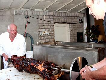 Herbert Fischer (links) hebt mit einem Helfer das fertige Spanferkel aus dem selbst gebauten Grill.  Fotos: Johanna Blum