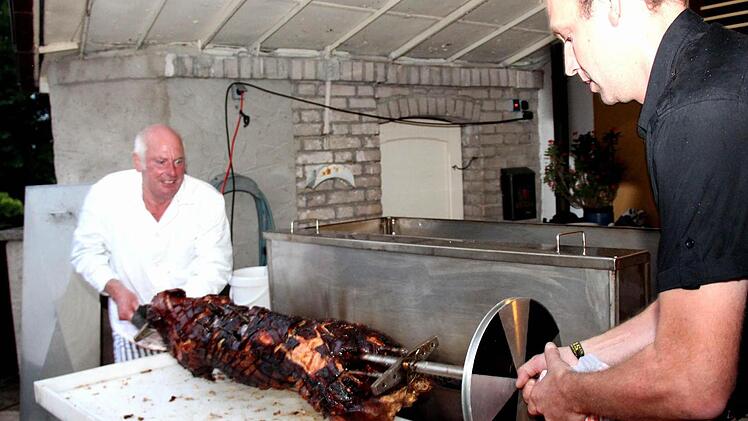 Herbert Fischer (links) hebt mit einem Helfer das fertige Spanferkel aus dem selbst gebauten Grill.  Fotos: Johanna Blum