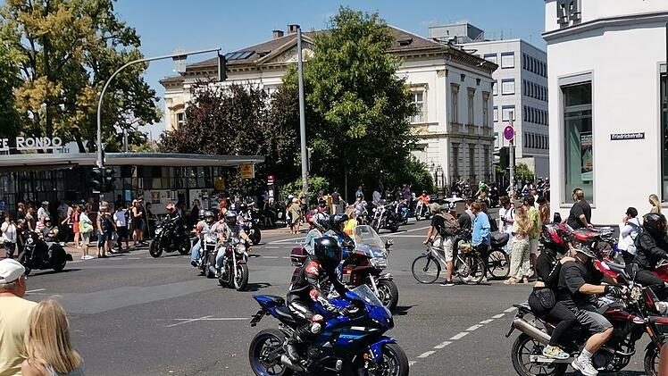 Motorradfahrer fahren bei strahlendem Sonnenschein durch eine belebte Kreuzung, während Menschen zuschauen. Das Event "Toy Run" unterstützt kranke Kinder und Jugendliche in Bamberg.