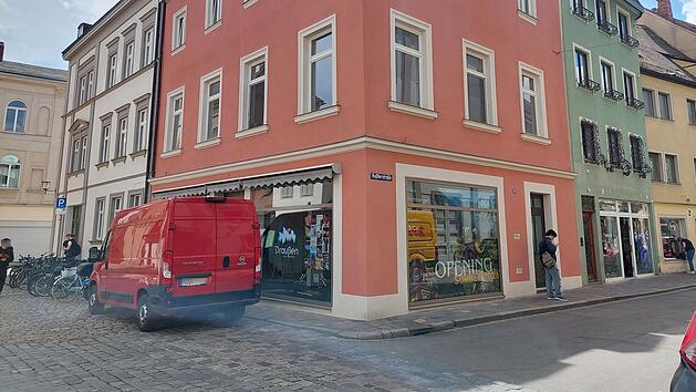 Ein rotes Geb&auml;ude an einer Ecke in der Bamberger Innenstadt. Im Fenster ein Schild mit "Opening Sommer 2023". Ein roter Lieferwagen steht auf der Kopfsteinpflasterstra&szlig;e.
