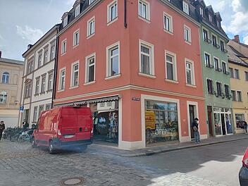 Ein rotes Geb&auml;ude an einer Ecke in der Bamberger Innenstadt. Im Fenster ein Schild mit "Opening Sommer 2023". Ein roter Lieferwagen steht auf der Kopfsteinpflasterstra&szlig;e.