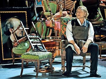 Der Bariton-Sänger Michael Volle als Hans Sachs in der Schusterstube des 2. Akts, hinter der sich das Wahnfried-Mobiliar des 1. Akts als Konkursmasse auftürmt.  Foto: Bayreuther Festspiele/Enrico Nawrath