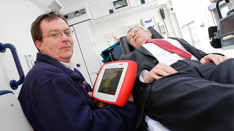 Johannes Arneth, Leiter der BRK-Rettungswache Scheßlitz, demonstriert mit Landrat Johann Kalb als Notfallpatient die Funktionsweise des neuen Tablets, mit dem der Rettungsdienst wichtige Daten schon im Voraus an die Klinik senden kann. Foto: Matthias Hoch
