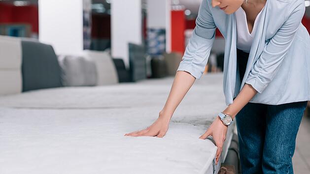 Teilansicht einer Frau, die eine orthopädische Matratze in einem Möbelgeschäft berührt