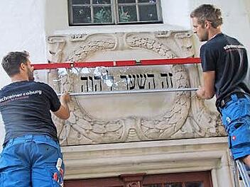 Steffen Voigt und Robin Habermann bringen über dem Eingang der St.-Nikolaus-Kapelle die Glasplatte mit dem ursprünglichen Text der dort befindlichen Sandsteinkartusche an.  Foto: Martin Koch